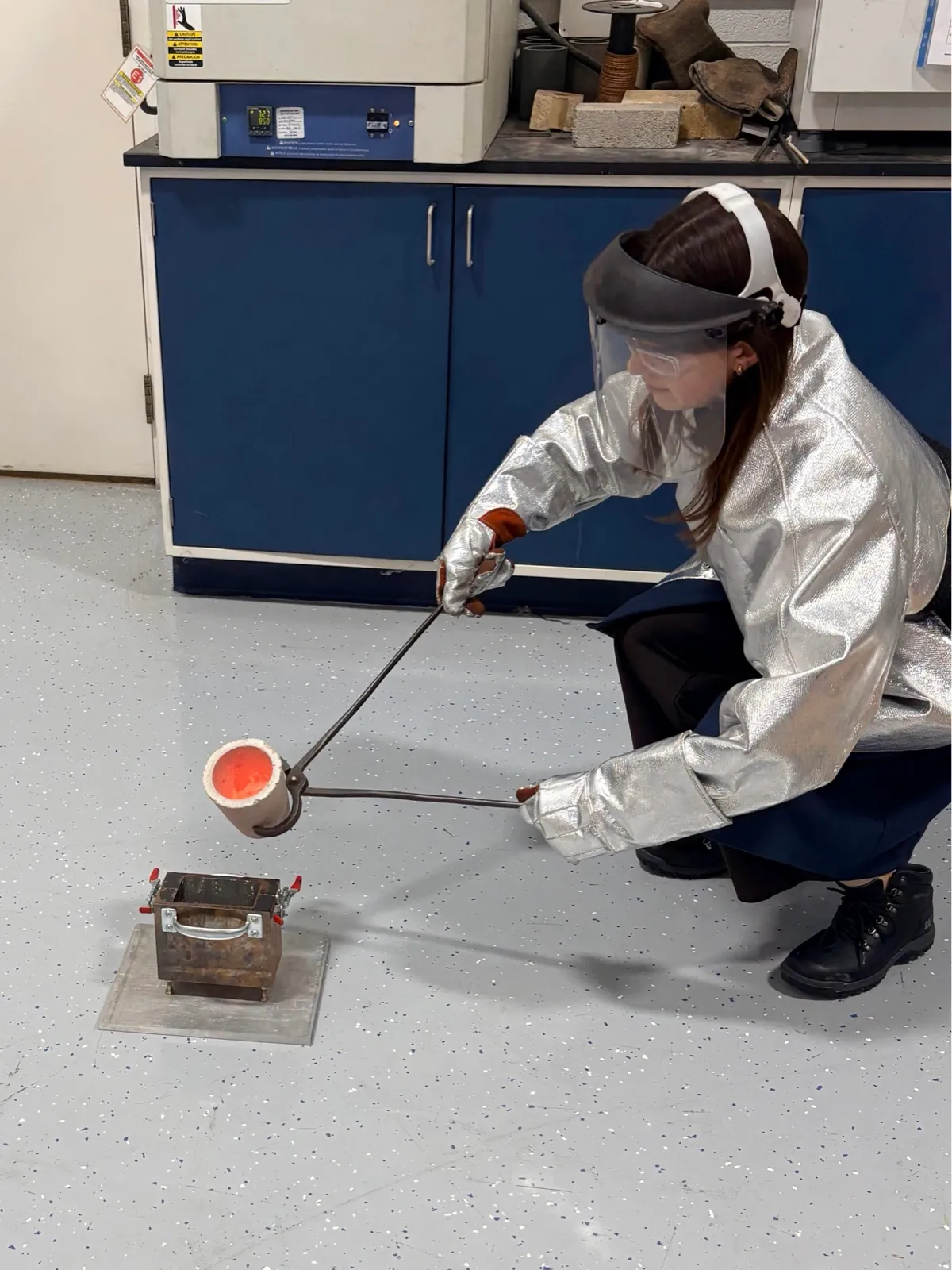 Daniela using protective equipment while handling a glowing crucible during a casting process
